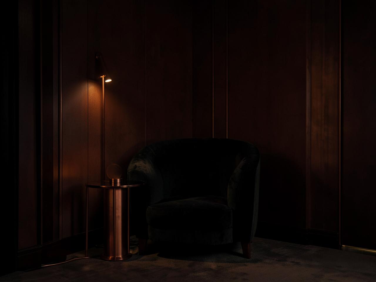 Dimly lit lounge corner with a velvet armchair and copper lamp