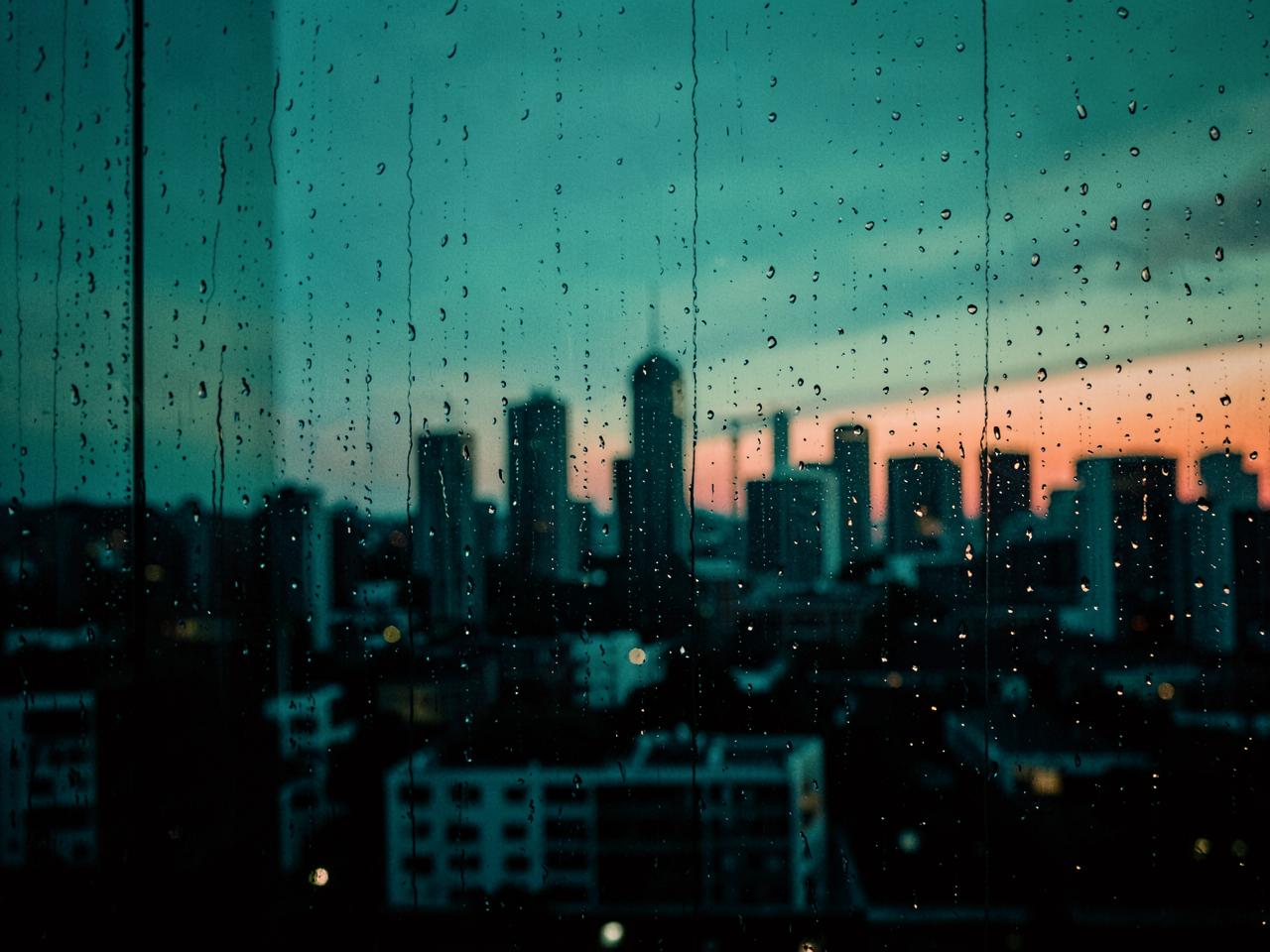 City skyline at dusk seen through a rain-flecked window